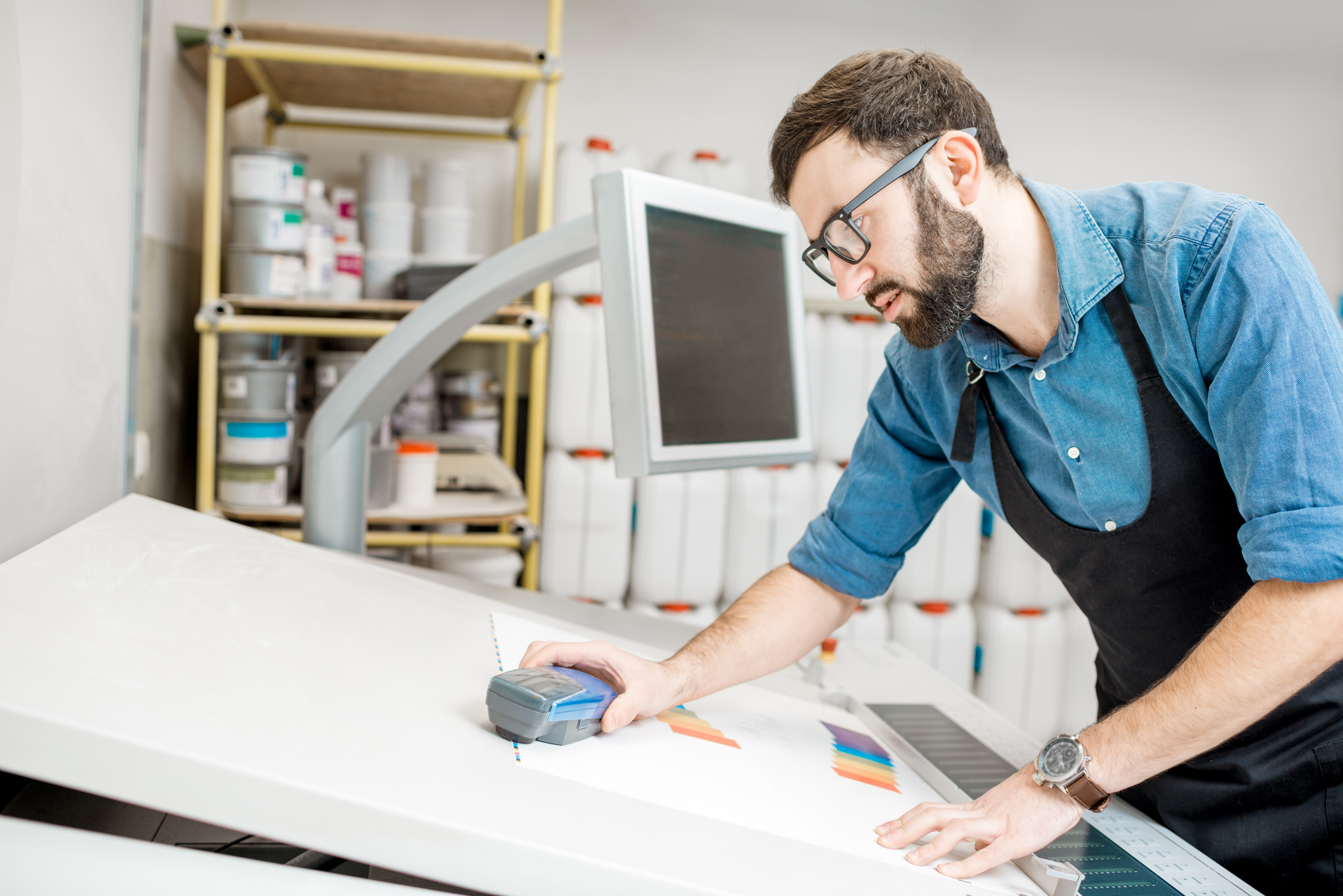 Man worker measuring printing color with spectrometer on the operating desk of the printing plant